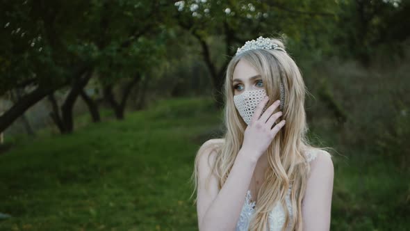 portrait of the bride in a mask posing. Beautiful young bride in a wedding dress in the park. She ha