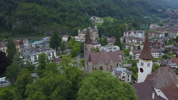 Aerial orbit of Catholic and Protestant Churches in Interlaken village near lake, surrounded by fore