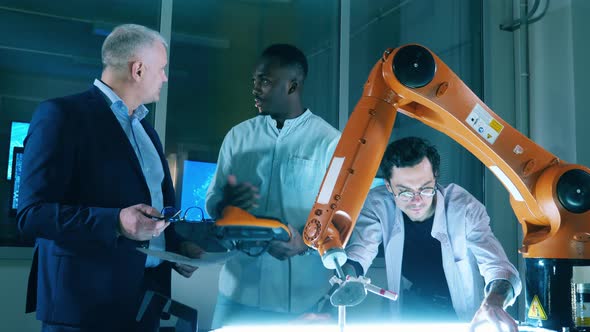 Male Researchers Are Talking While Operating a Robotic Arm