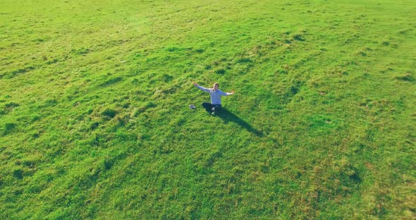 Low Orbital Flight Around Man on Green Grass with Notebook Pad at Yellow Rural Field