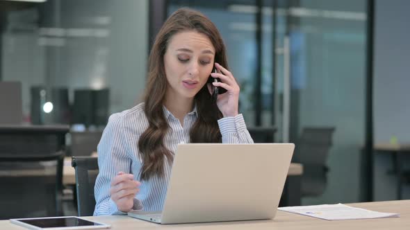 Young Businesswoman Talking on Smartphone while using Laptop