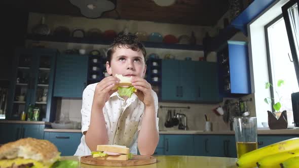 Boy bites a delicious sandwich in the kitchen home and has Breakfast