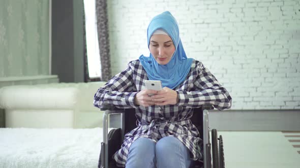 Beautiful Young Woman in Hijab Is Disabled Wheelchair Uses the Phone