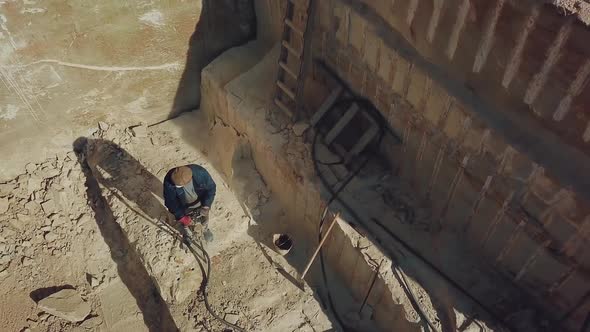 a man is drilling stones with using power tool in a sand quarry. Camera motion up