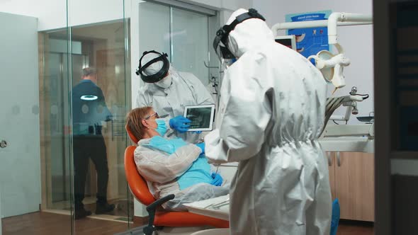 Dentist in Coverall Showing on Tablet Dental Xray Reviewing It