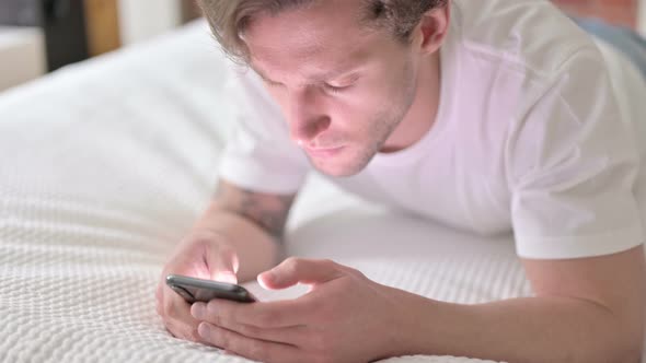 Ambitious Young Man Scrolling on Smartphone in Bed