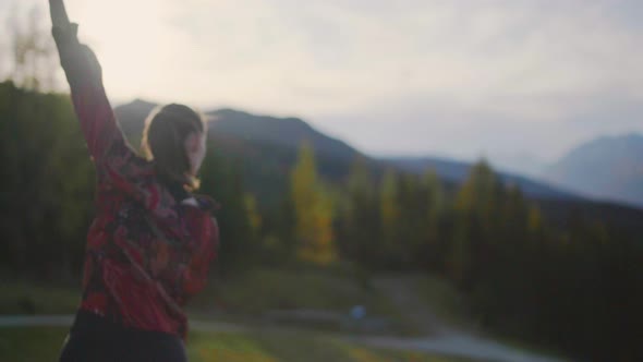 Slow motion of a young woman dancing on a wooden platform at sun set, golden hour. Alpine mountains