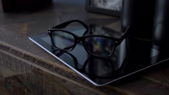 Glasses in Black Rim Lying on a Tablet on a Wooden Dresser in the Room Close Up