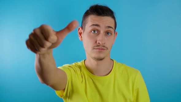 Young Man on a Blue Background Grimacing with His Thumbs Down Giving a Negative Opinion Judging a