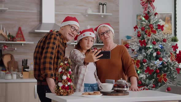 Granddaughter Taking Selfie Using Smarphone with Grandparents During Christmas Holiday Celebration