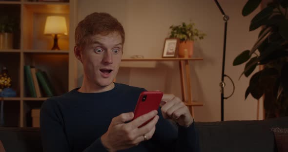 Crop View of Excited Red Haired Man Scrolling Phone Screen While Sitting on Sofa at Home