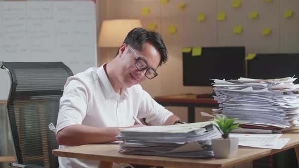 Smiling Asian Man Enjoys Working With Documents At The Office