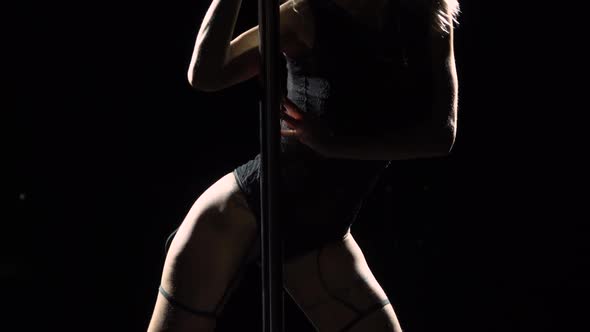 Young Sexy Slim Woman Dancing Near a Pole on a Black Studio Background