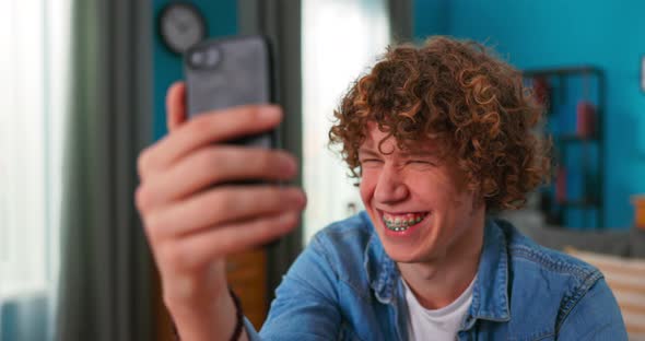 Young Brunette Curly Hair Man Sitting at Desk in Living Room Using Smartphone