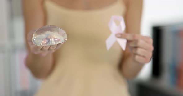 Woman Holding Silicone Breast Implant and Pink Ribbon in Clinic  Movie