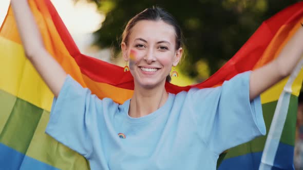 A close-up view of a smiling woman with colorful make-up holding a colorful flag during pride gay pa