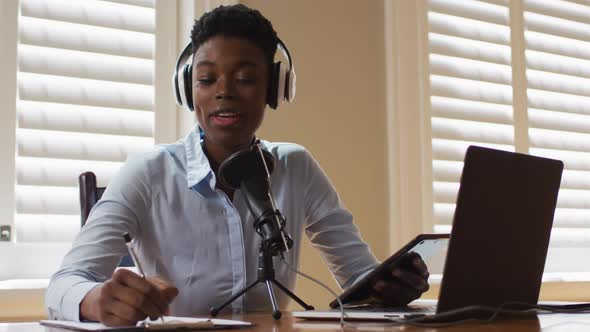 African american woman wearing headphones taking notes and singing at home