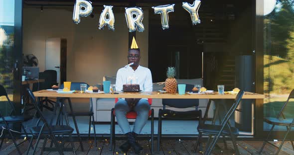 Birthday Party on Quarantine. Sad Lonely African Young Man Blows Whistle Alone Celebrating with Cake