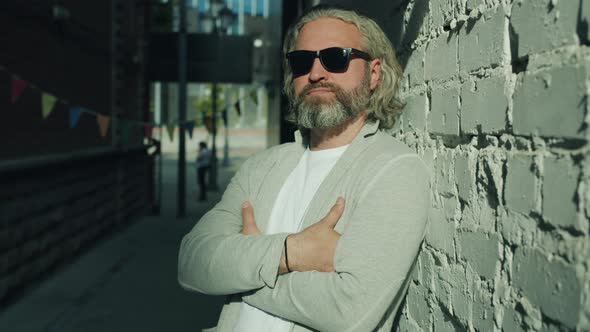 Portrait of Stylish Man Wearing Sunglasses Standing Outdoors with Arms Crossed with Brick Wall in