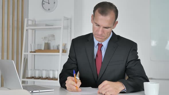 Middle Aged Businessman Writing Documents in Office