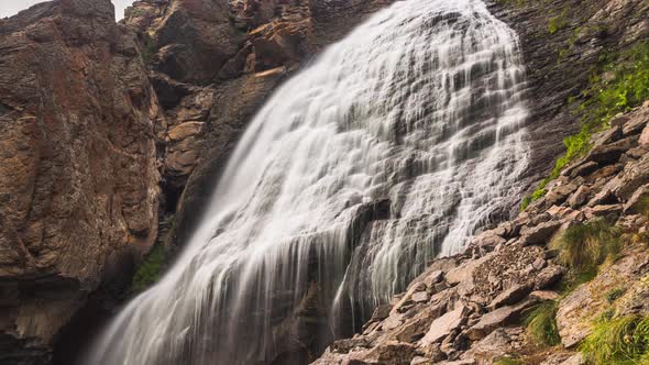 White Waterfall Over Cliff with Rocks Under Bright Sunlight