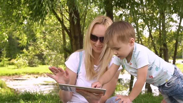 Happy Mother and Her Little Son Enjoying Playing on Tablet Computer in the Park. Slow Motion