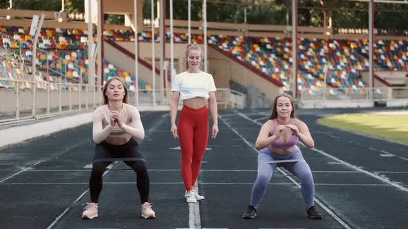 Sportswomen and Coach Doing Squats with Resistance Fitness Rubber Band on Stadium