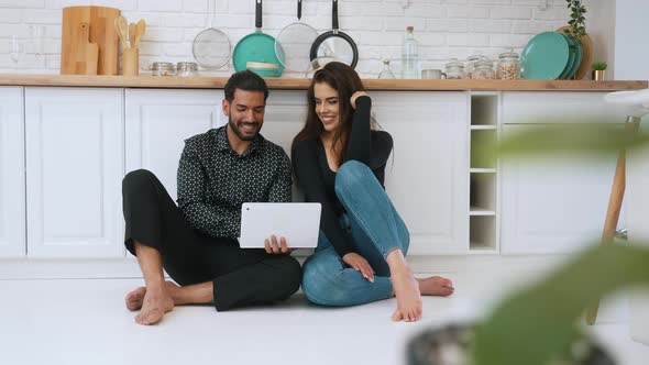 Attractive Happy Interracial Couple in Their 30s Sitting on a White Floor Crosslegged in a Kitchen