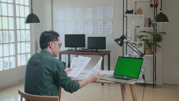 Creative Designer Works On A Storyboard, Looks At His Sketches With Mock Up Green Screen Laptop