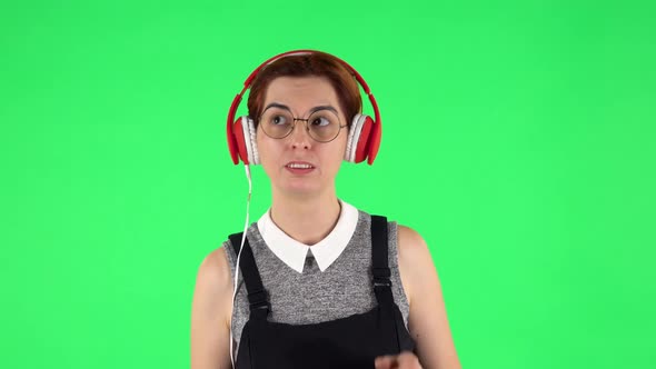 Portrait of Funny Girl in Round Glasses Is Dancing and Enjoying Music in Big Red Headphones. Green