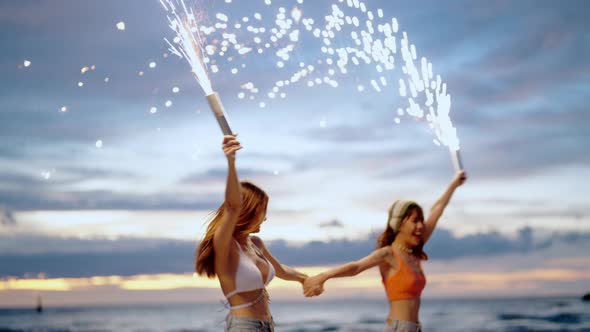 4K Young Asian woman friends playing sparkler fireworks together on the beach at summer sunset.