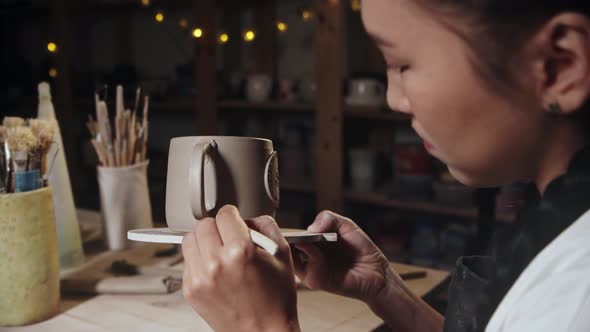 Young Woman Potter Smears the Clay on the Foundation on the Cup Handle Using a Tool