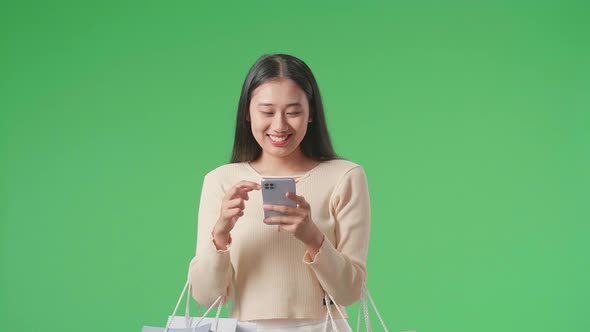 Woman With Shopping Bags Use Mobile Phone And Smile While Walking In Front Of Green Screen