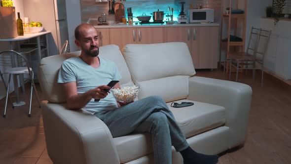 Man with Beard Watching Tv Show Using Remote Control to Change Channels on Television