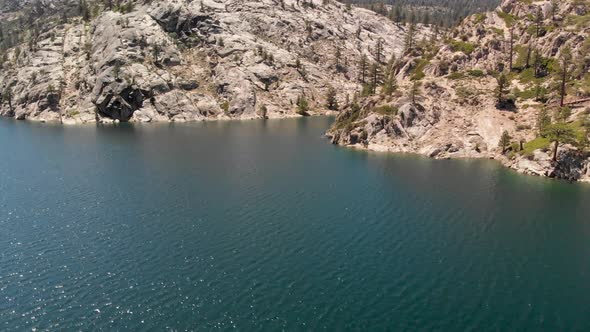 Fast aerial shot of pine trees and granite on the shore of a high Sierra lake in California.