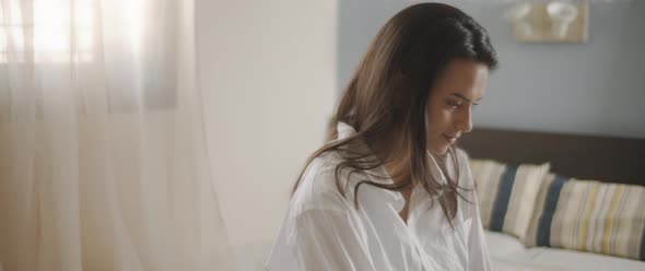 A close up of a young woman in white shirt working from home in her bedroom. 