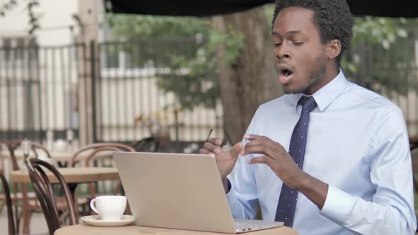 African Businessman Celebrating on Laptop in Outdoor Cafe