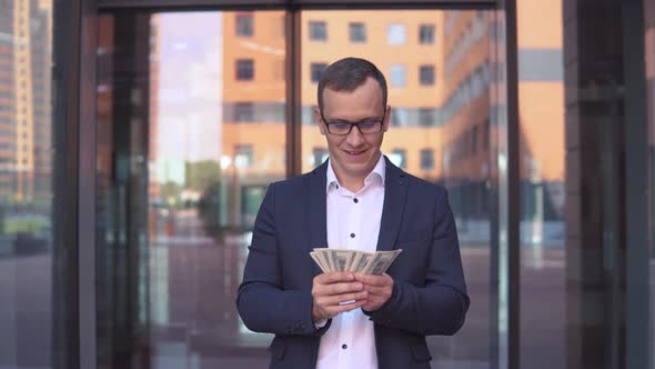 A Wealthy Young Businessman Counts Money Standing Near the Business Center Having a Good Mood