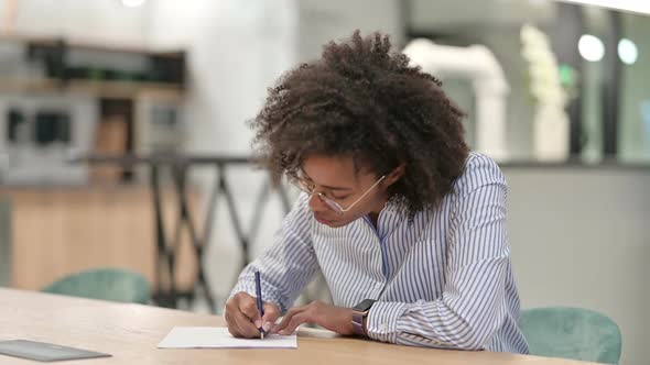 Pensive African Businesswoman Writing on Paper in Office