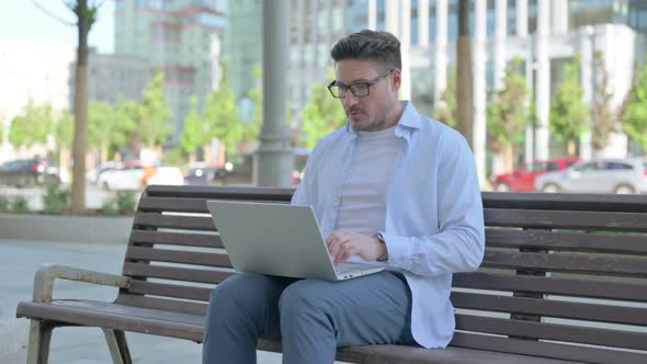 Man with Laptop Looking at Camera While Sitting Outdoor on Bench