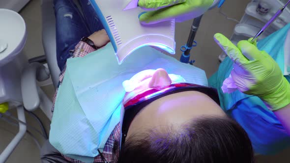 Young Woman with an Expander in Mouth and Red Protective Glasses Getting UV Whitening at the Dentist