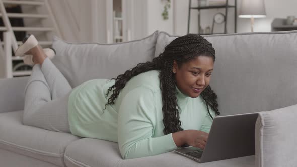 Young African-American Woman Lying on Sofa with Laptop