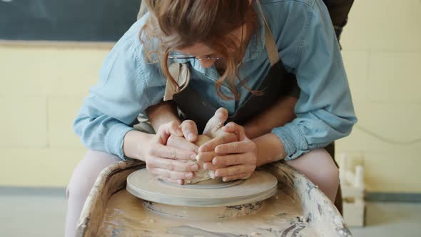 Man and Woman Making Pot on Throwing Wheel Shaping Clay Together in Workshop