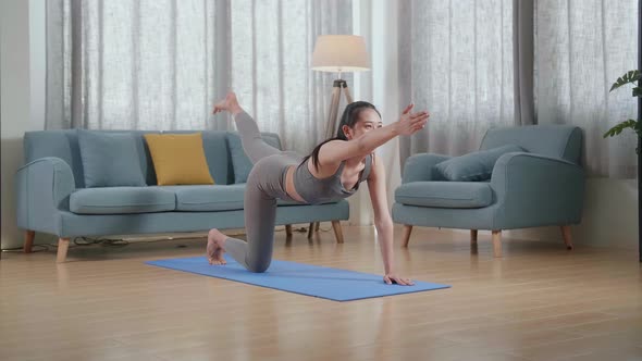 Asian Athletic Female In Sports Clothes Doing Yoga In Balancing Table Pose On The Mat At Home