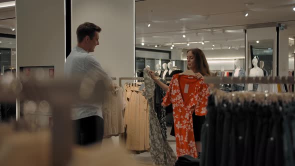 Caucasian Woman in the Store Asks the Guy's Advice Choosing Between Two Dresses