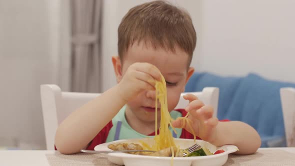 Small Child Is Sitting at a Table in a Bib and Eat His Own Spaghetti, the Cute Baby Eats Willingly