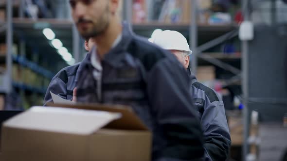 Young and Senior Caucasian Men Discussing Logistics As Middle Eastern Loader Passing with Box at