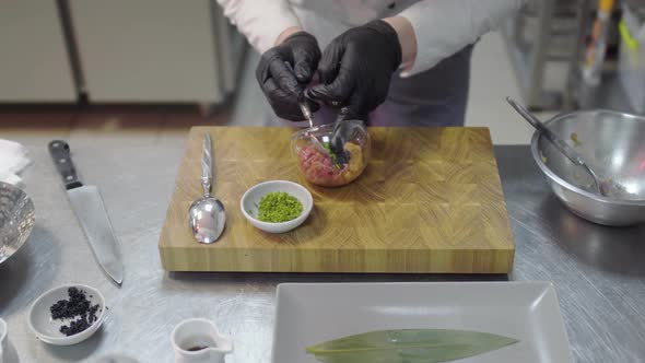 Chef in Black Rubber Gloves Preparing Dish with Raw Tuna and Salmon in Modern Restaurant Kitchen