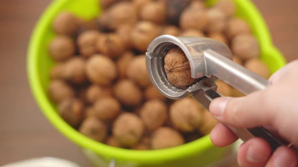 Nutcracker in Hand and Walnut Closeup Against the Background of a Bucket with Nuts