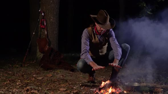 Cowboy Near the Fire in the Forest at Night